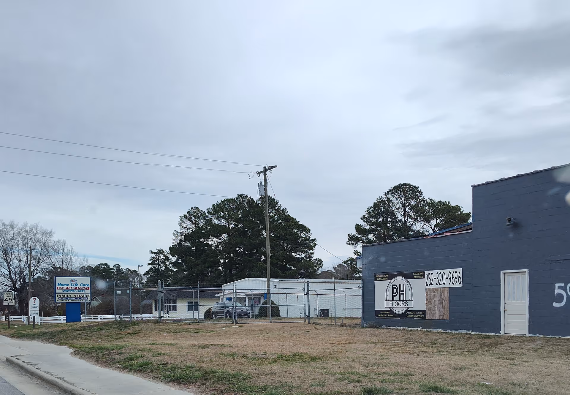 Blue commercial building with a chain-link fence and signs along a street.