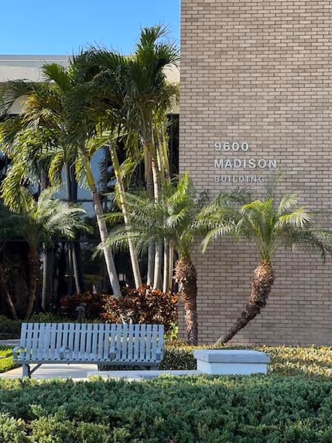Exterior view of a BAYADA building with palm trees and a blue bench.