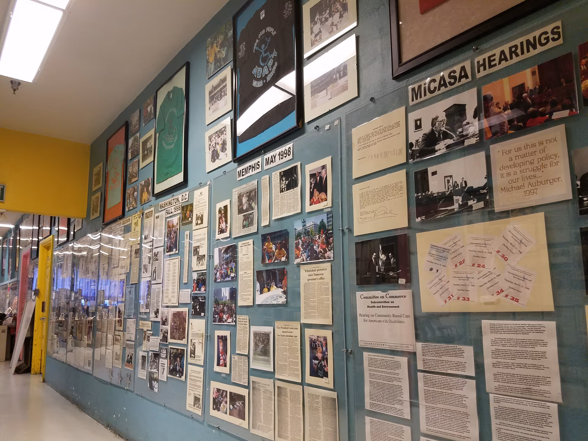 Blue hallway wall filled with framed photos and newspaper clippings.