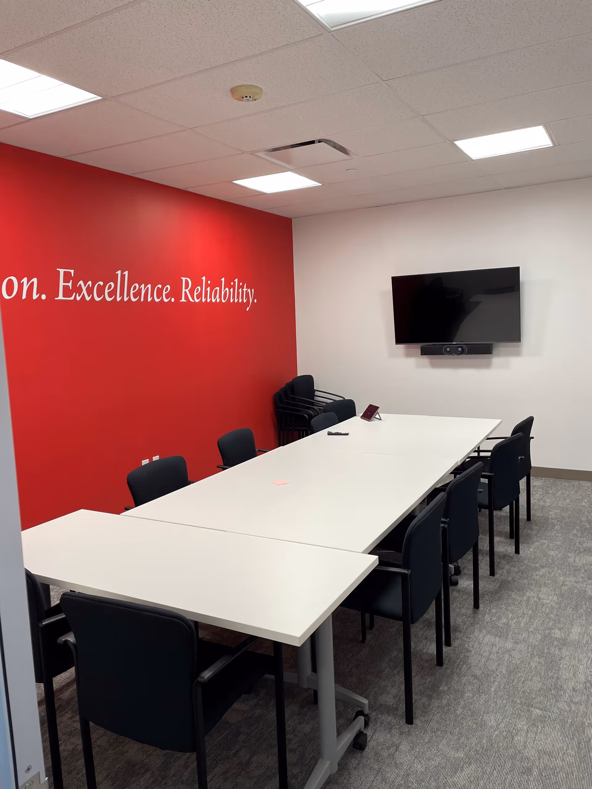 A conference room with a red accent wall, white tables, and a wall-mounted TV.