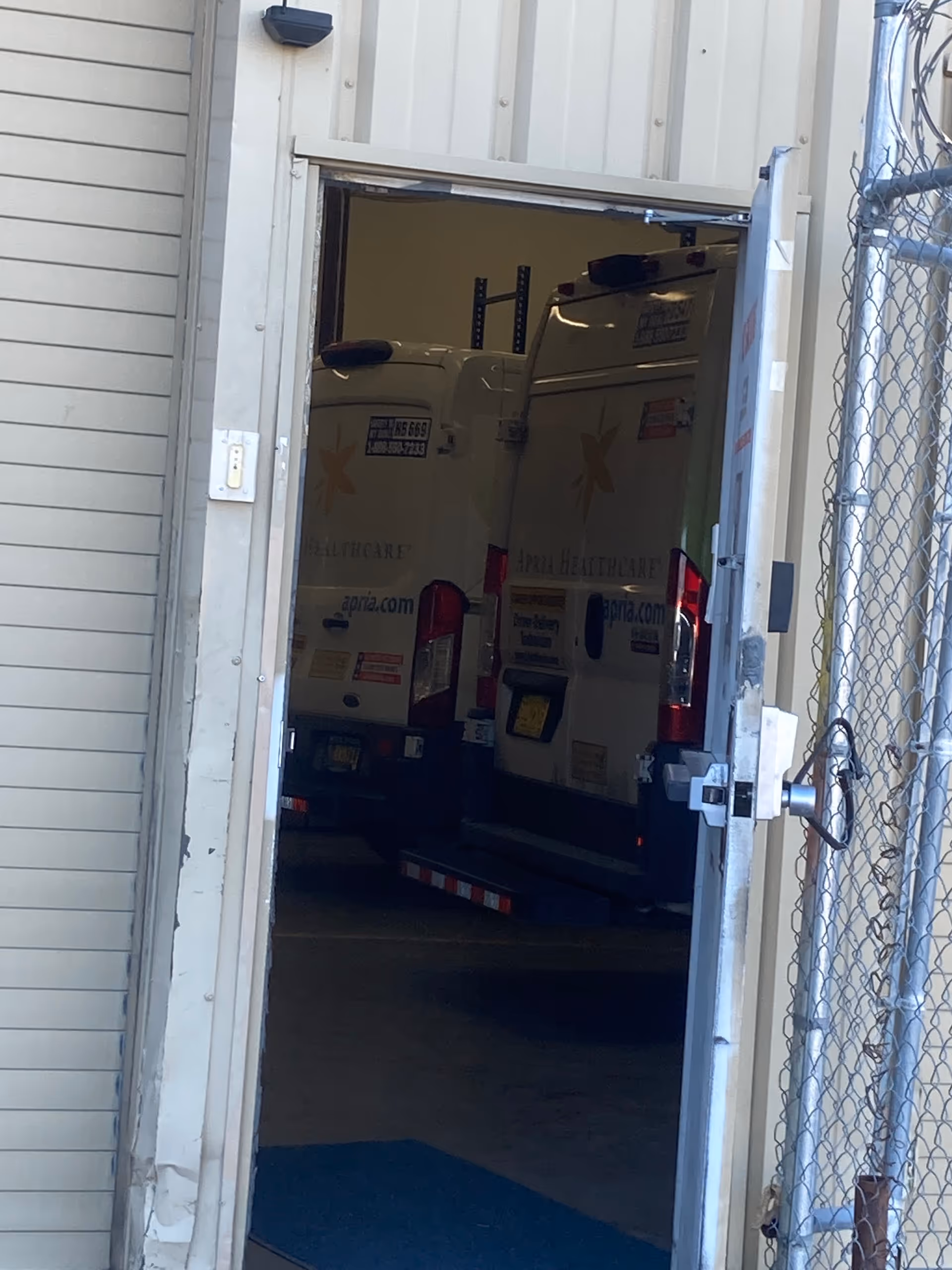 Open loading bay shows two Apria Healthcare vans inside a building.
