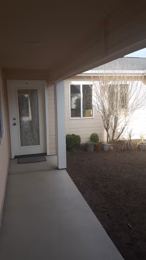 Covered walkway of a senior living facility leads to a glass entry door.