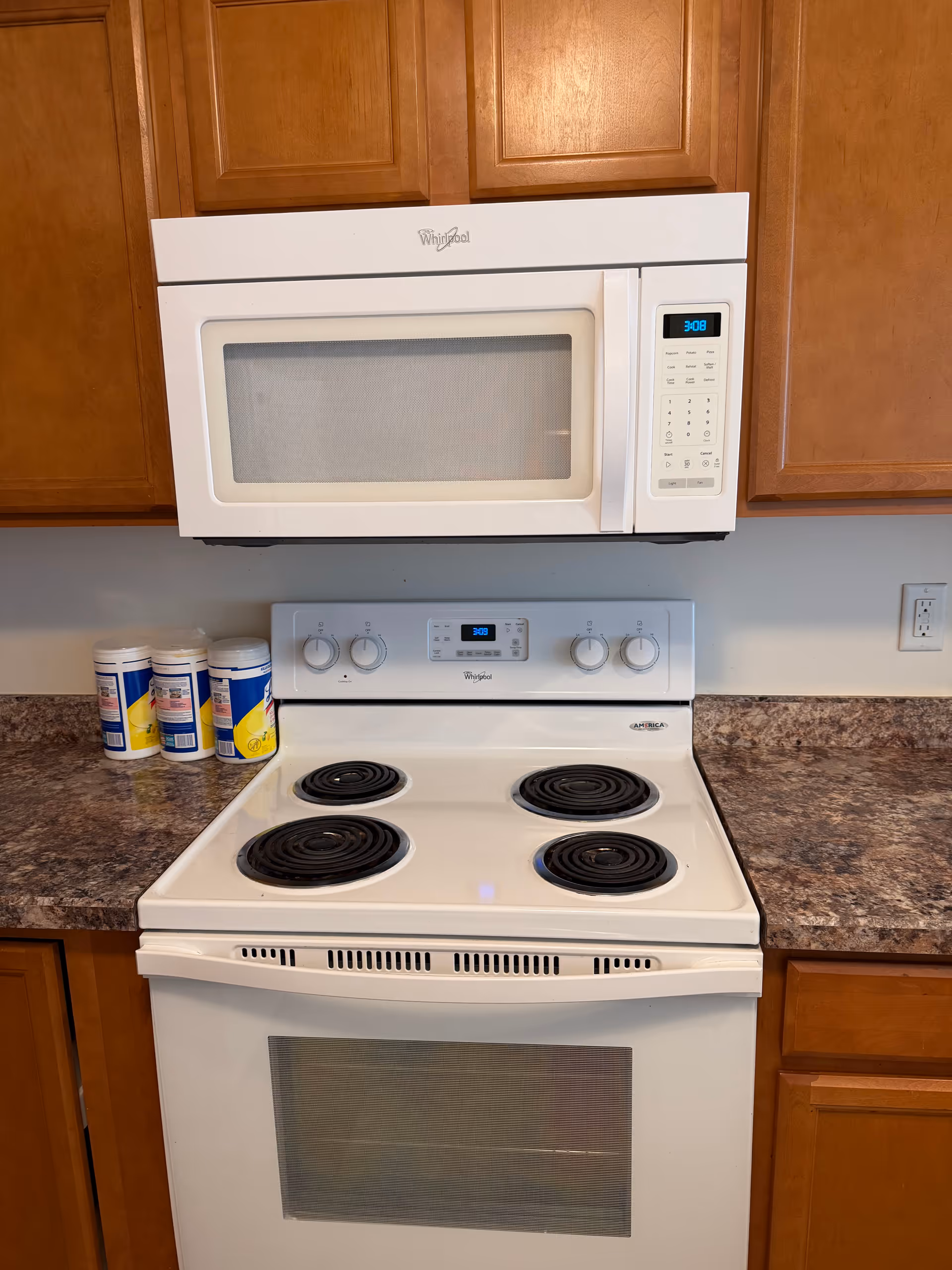 White electric stove and microwave in a kitchen with wooden cabinets and pill bottles.