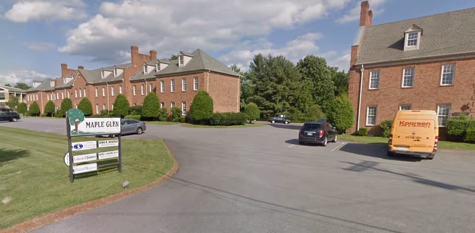 Brick senior living buildings line a curved driveway with parked cars and Maple Glen sign.