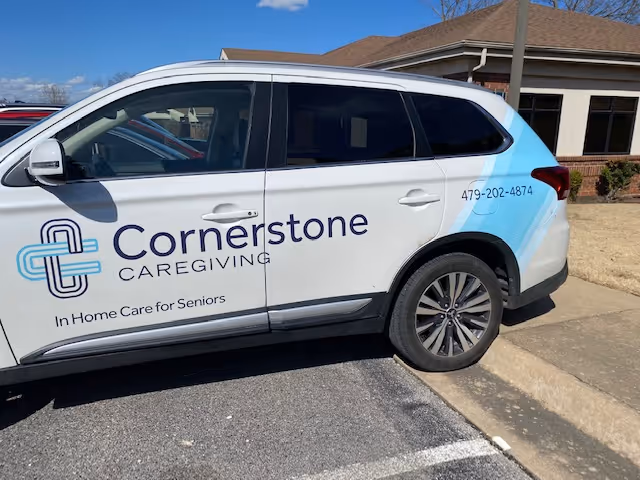 White Cornerstone Caregiving van parked outside a beige facility building.