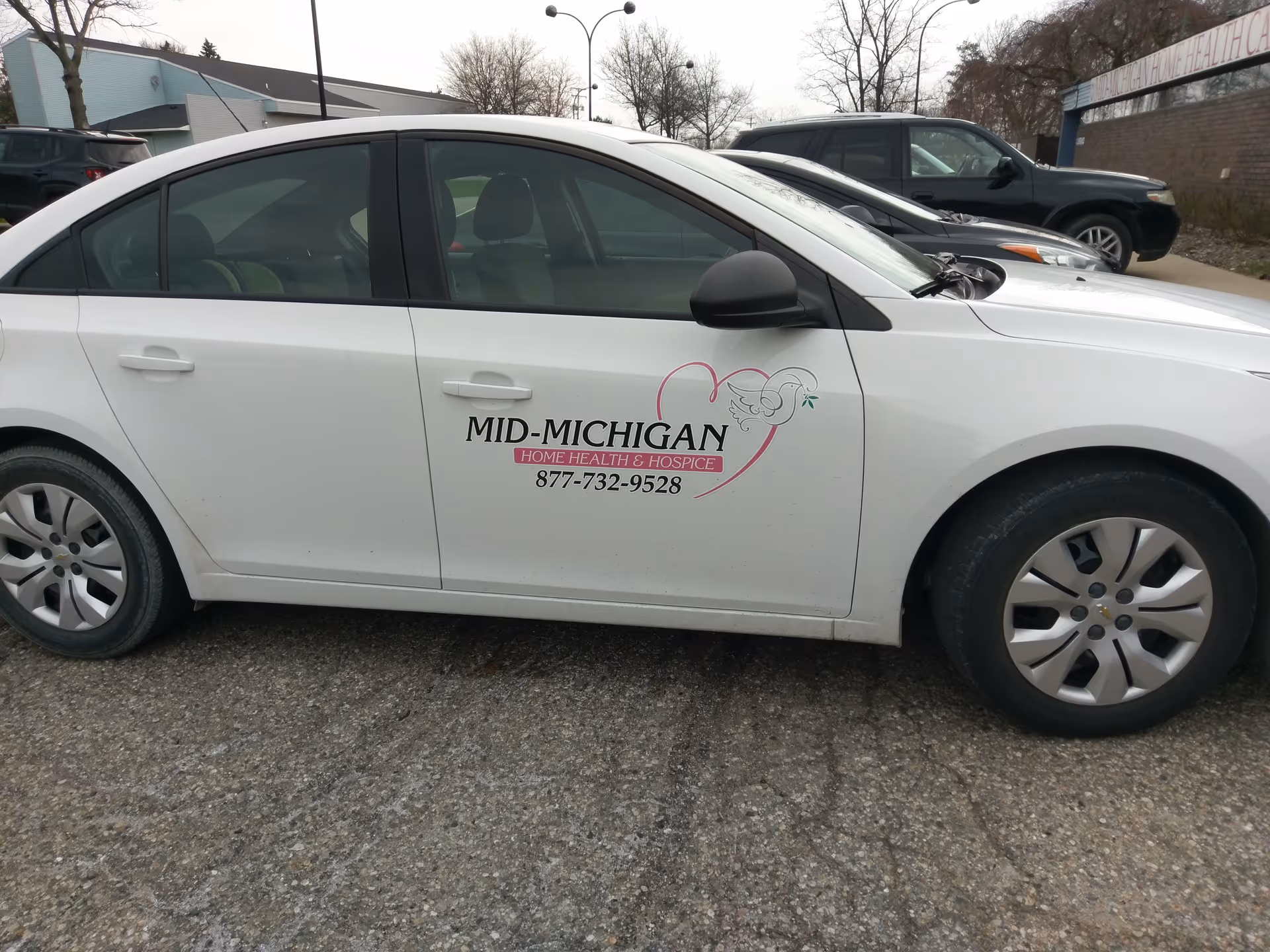 White sedan with Mid-Michigan Home Health & Hospice logo parked in a lot.