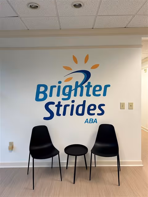 Interior wall with Brighter Strides ABA logo, three black chairs, and a small table.