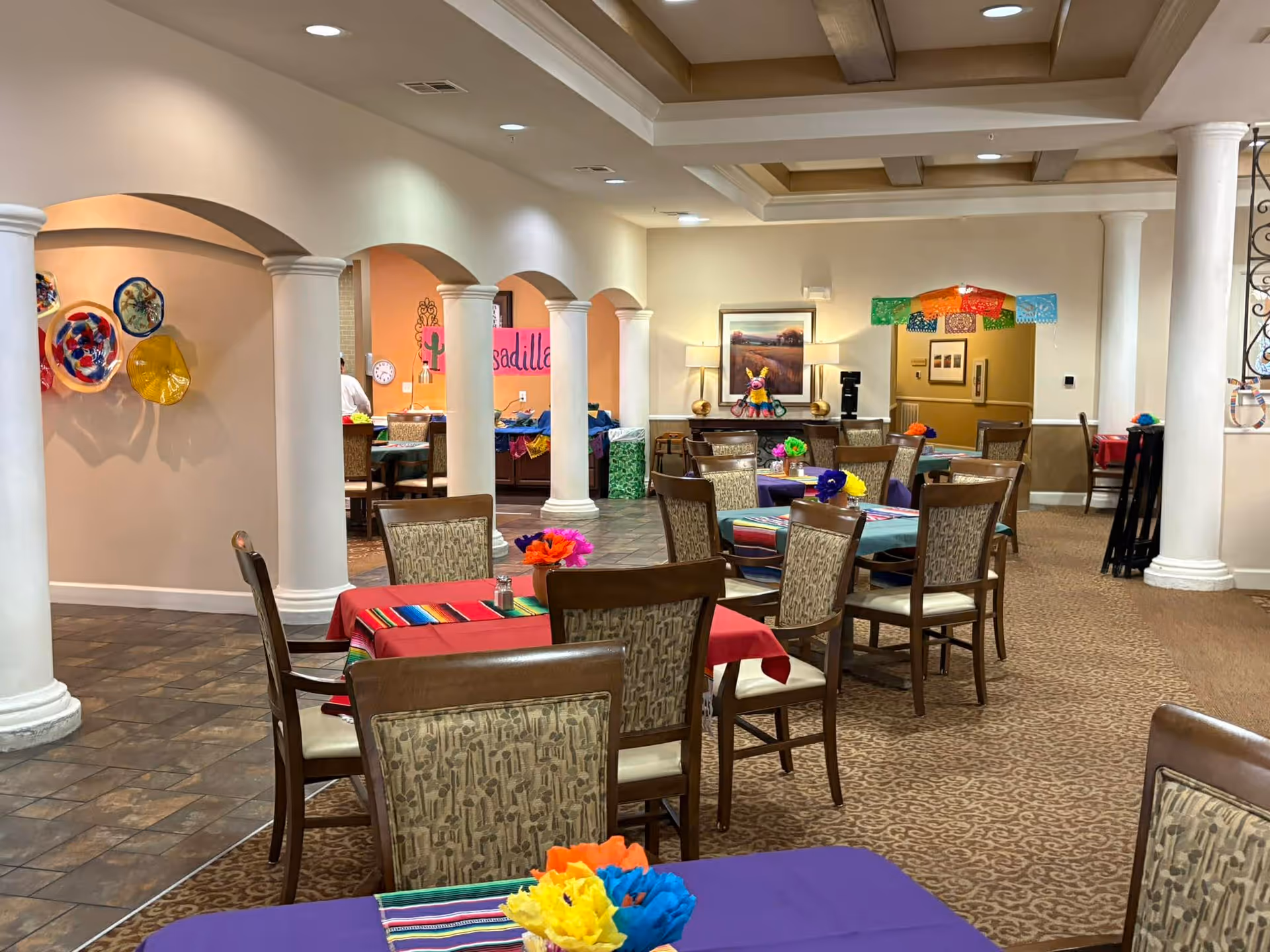 A spacious dining room with colorful tablecloths, chairs, and decorative banners.