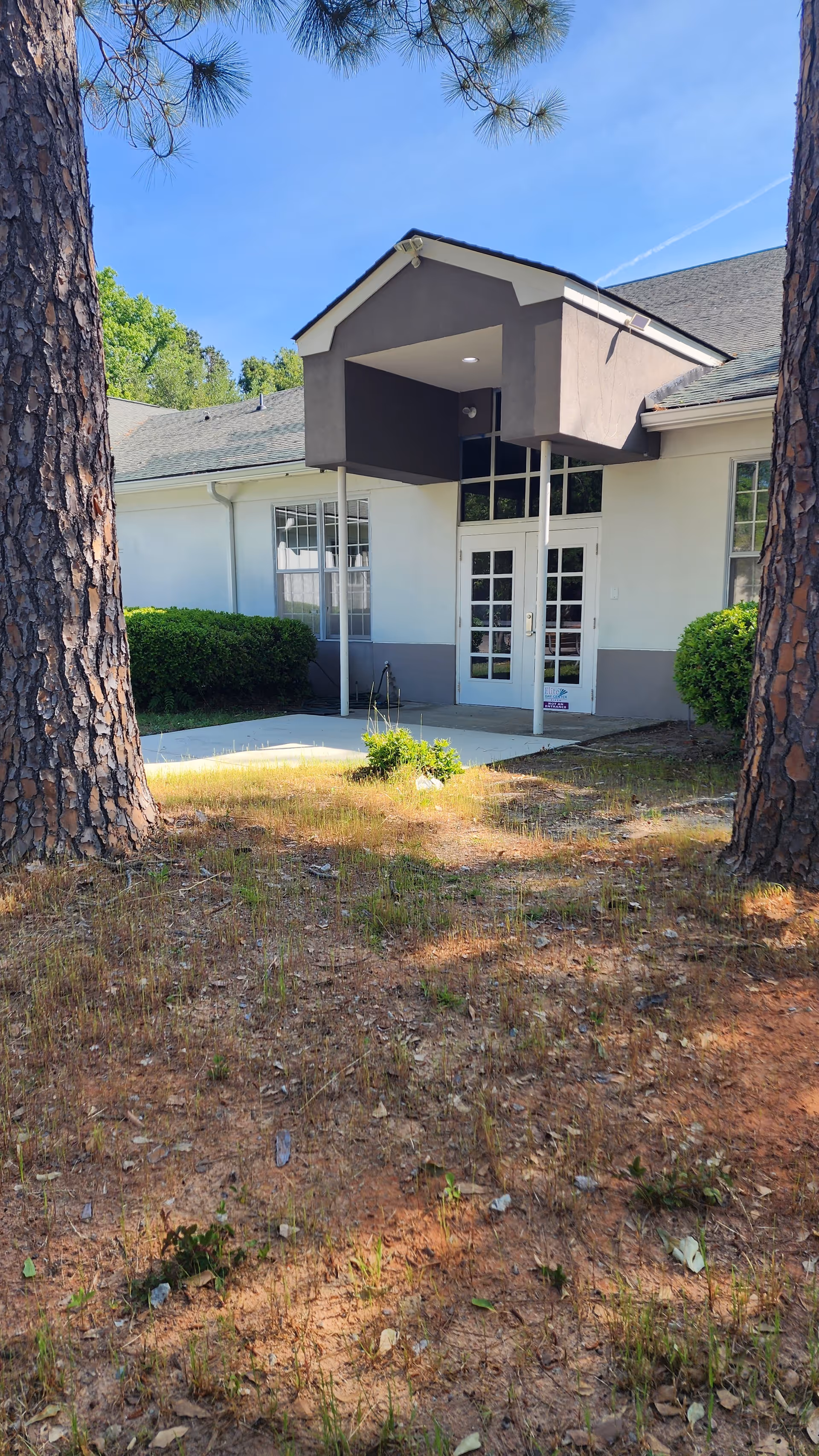 Exterior view of the Elite Home Care entrance with glass doors and surrounding shrubs.