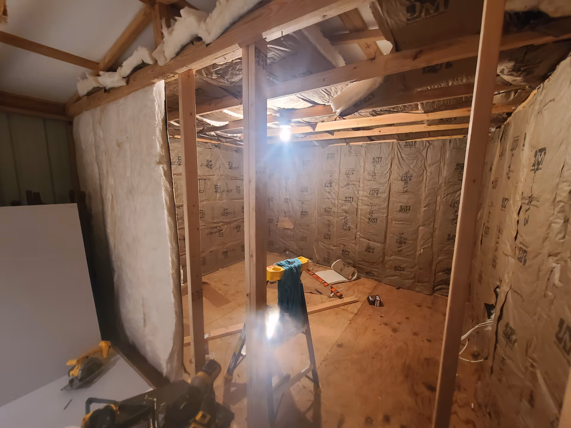 Unfinished interior renovation with exposed studs, insulation, and scattered construction tools.