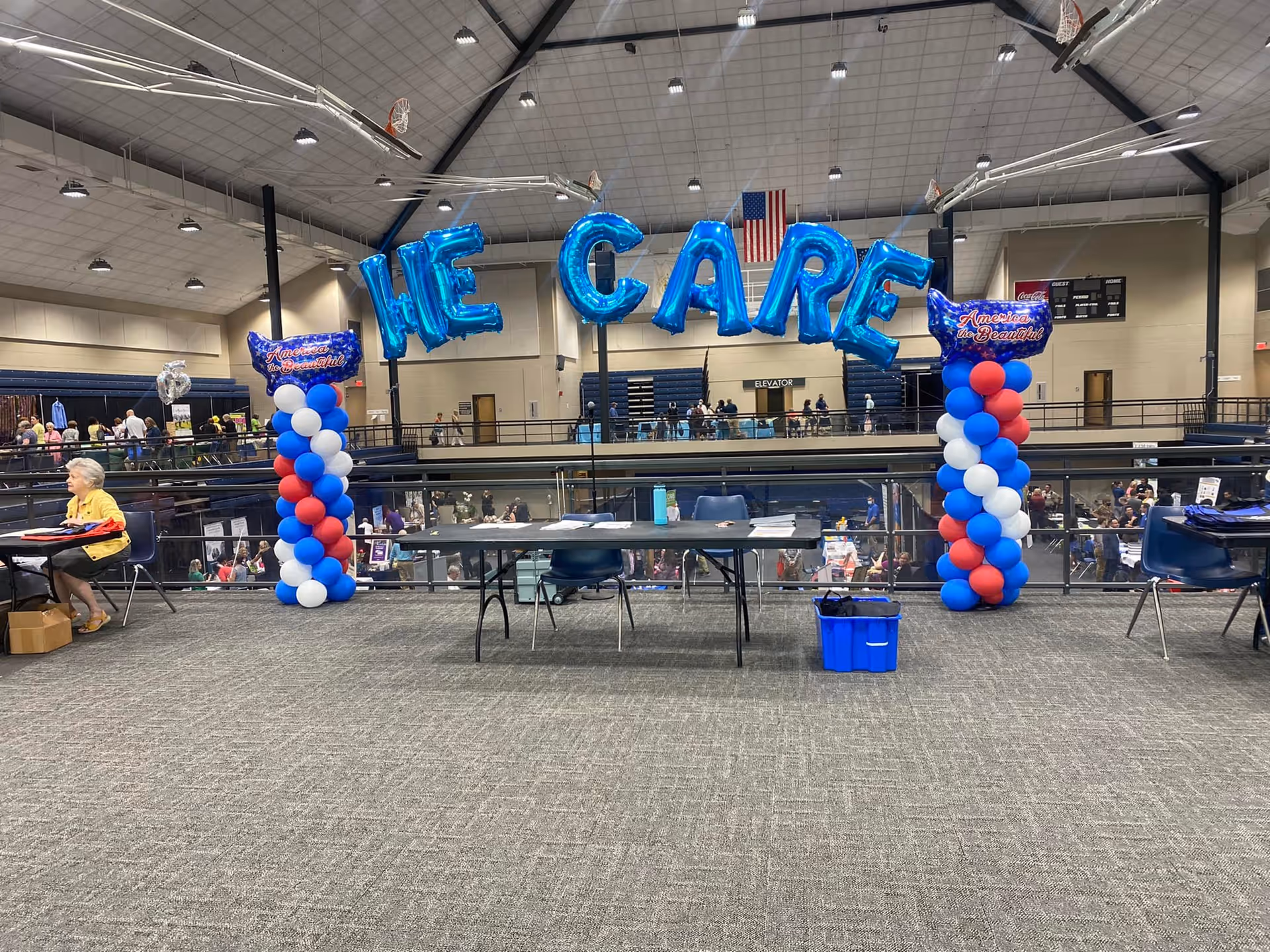 Indoor hall features large blue WE CARE balloons and attendees at a Visiting Angels event.