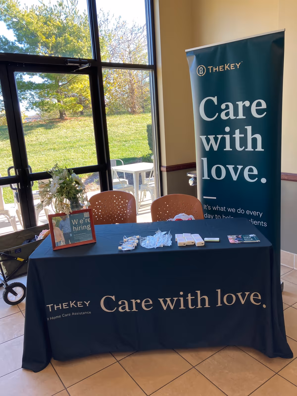 Indoor lobby with a TheKey banner reading Care with love, a table, chairs, and large windows.
