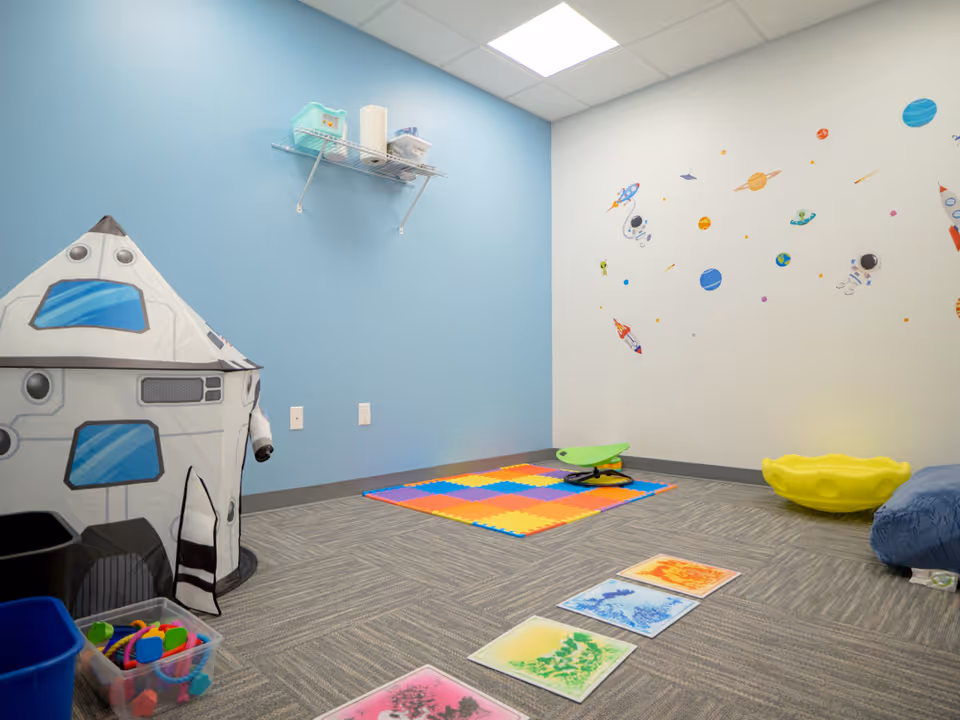 Space-themed children's playroom with rocket tent, colorful mats, and wall decals.