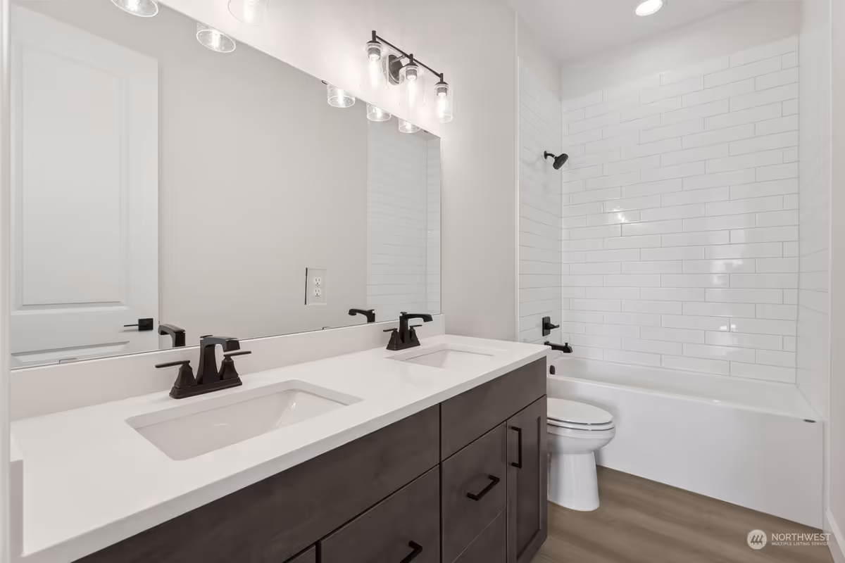 Double-sink bathroom with white countertops, dark cabinetry, toilet, and tiled shower.