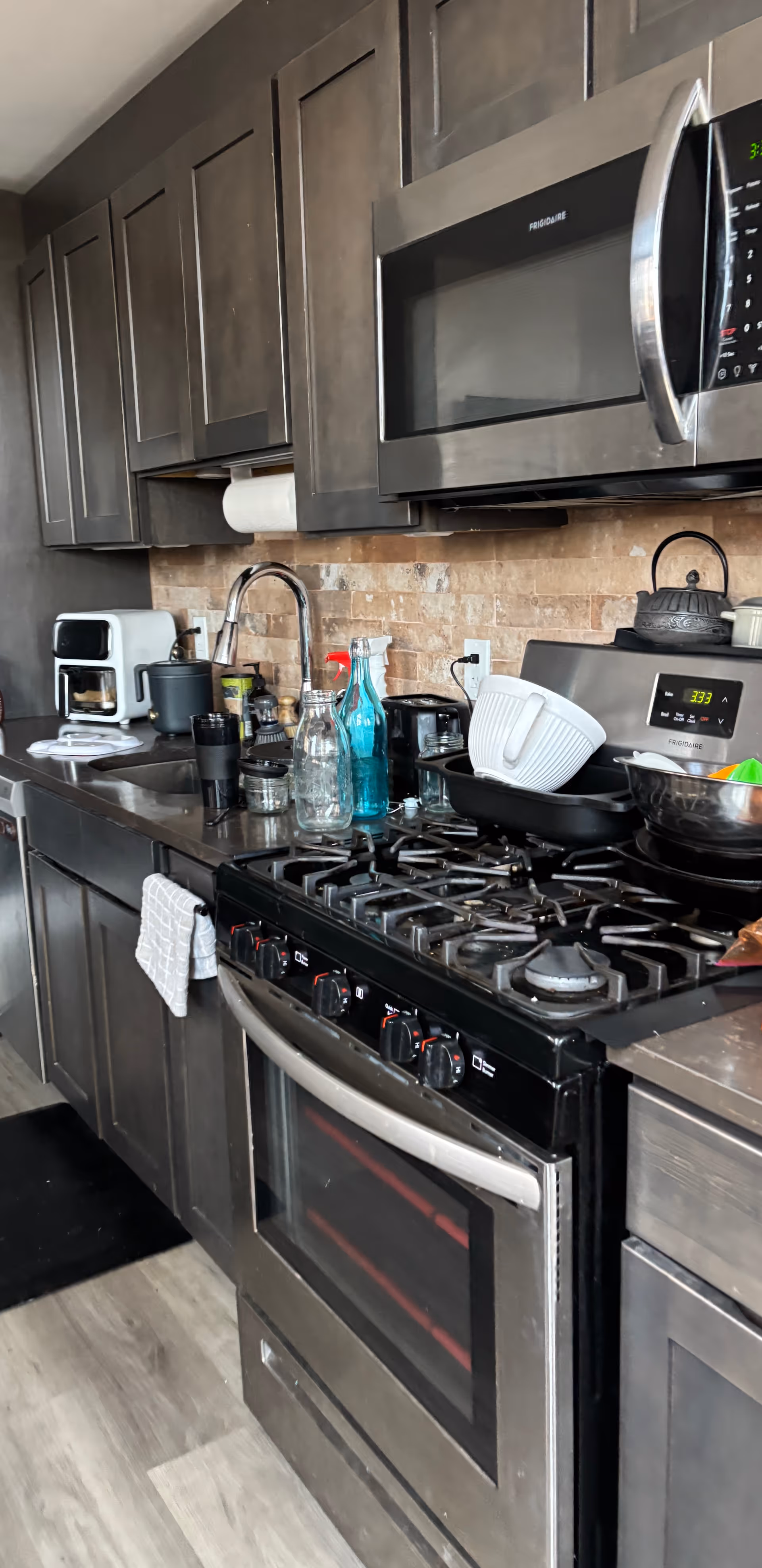 Modern kitchen with dark cabinets, stainless steel stove and microwave, and dishware on counter.