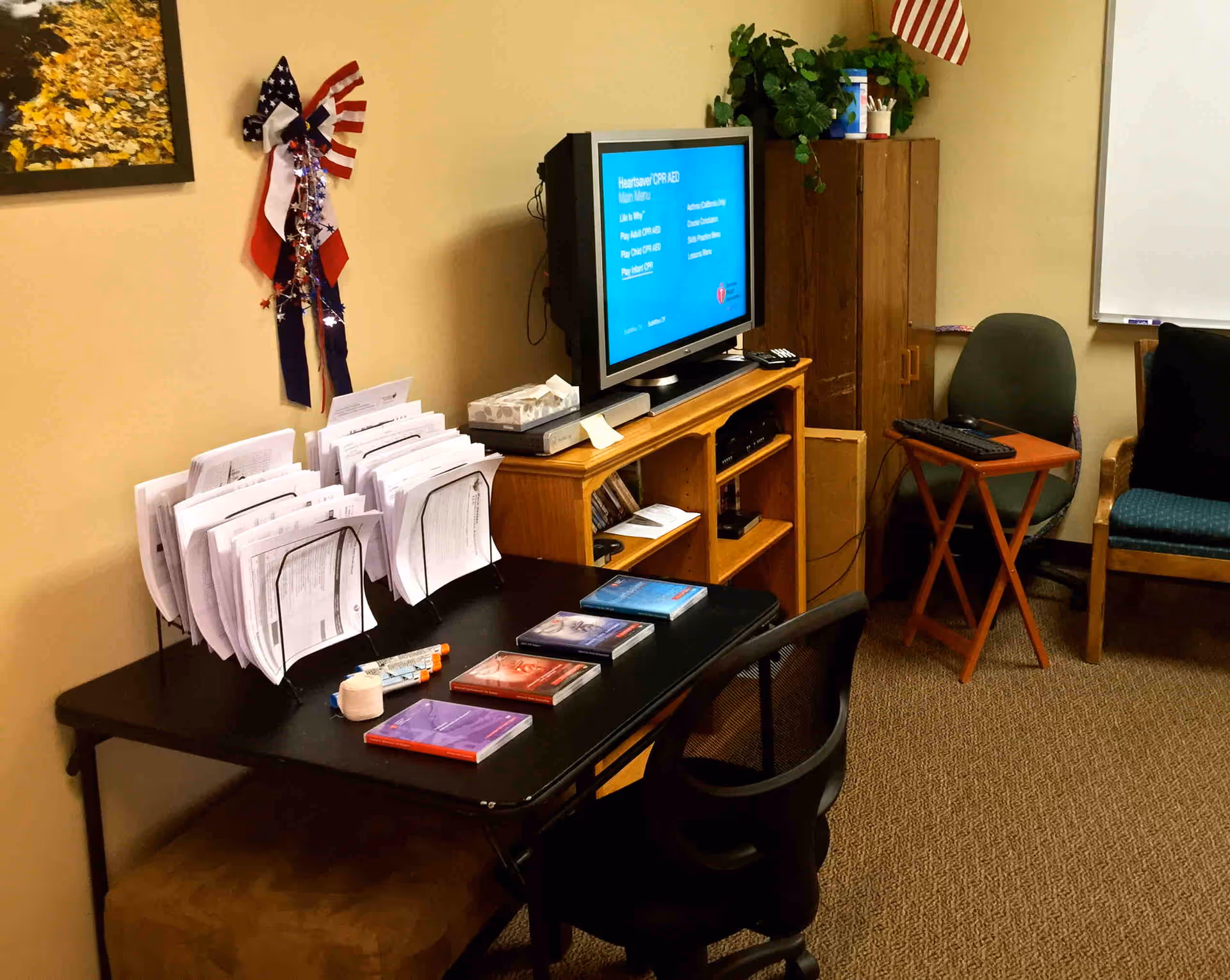 Office workspace in a senior facility with desk, papers, TV, and chairs.