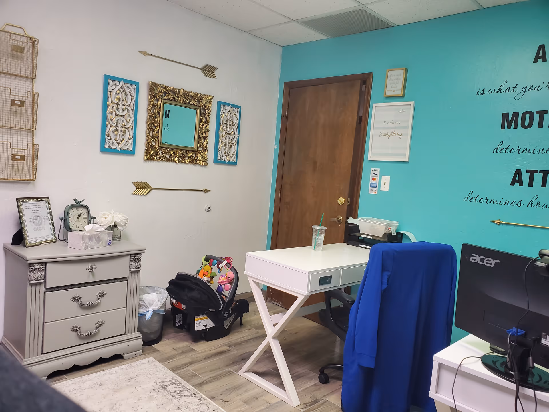 Bright office area with teal wall, desk, chair, and decorative wall art near door