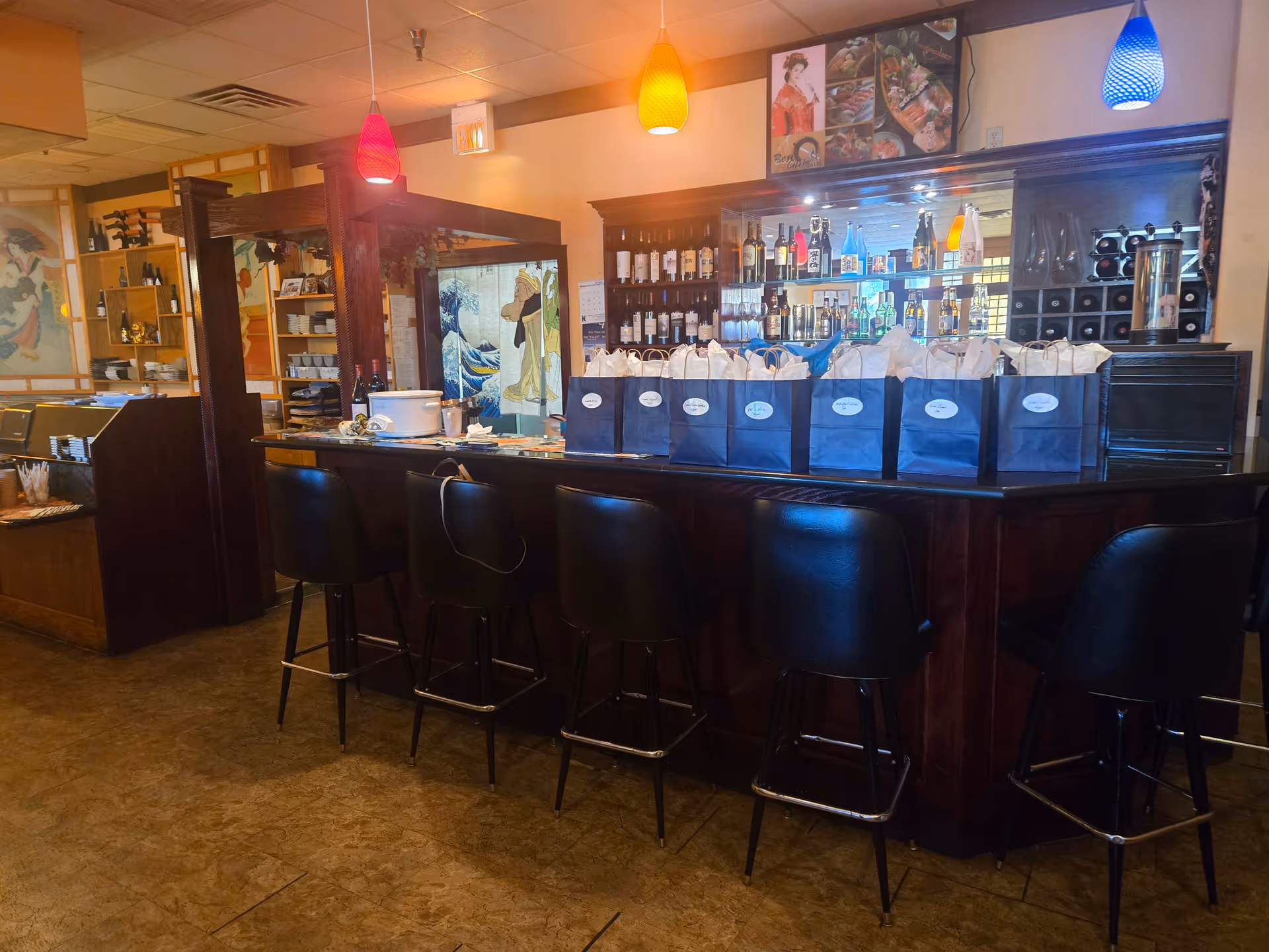 Interior bar area with stools, bottles, and blue gift bags on a dark wooden counter.