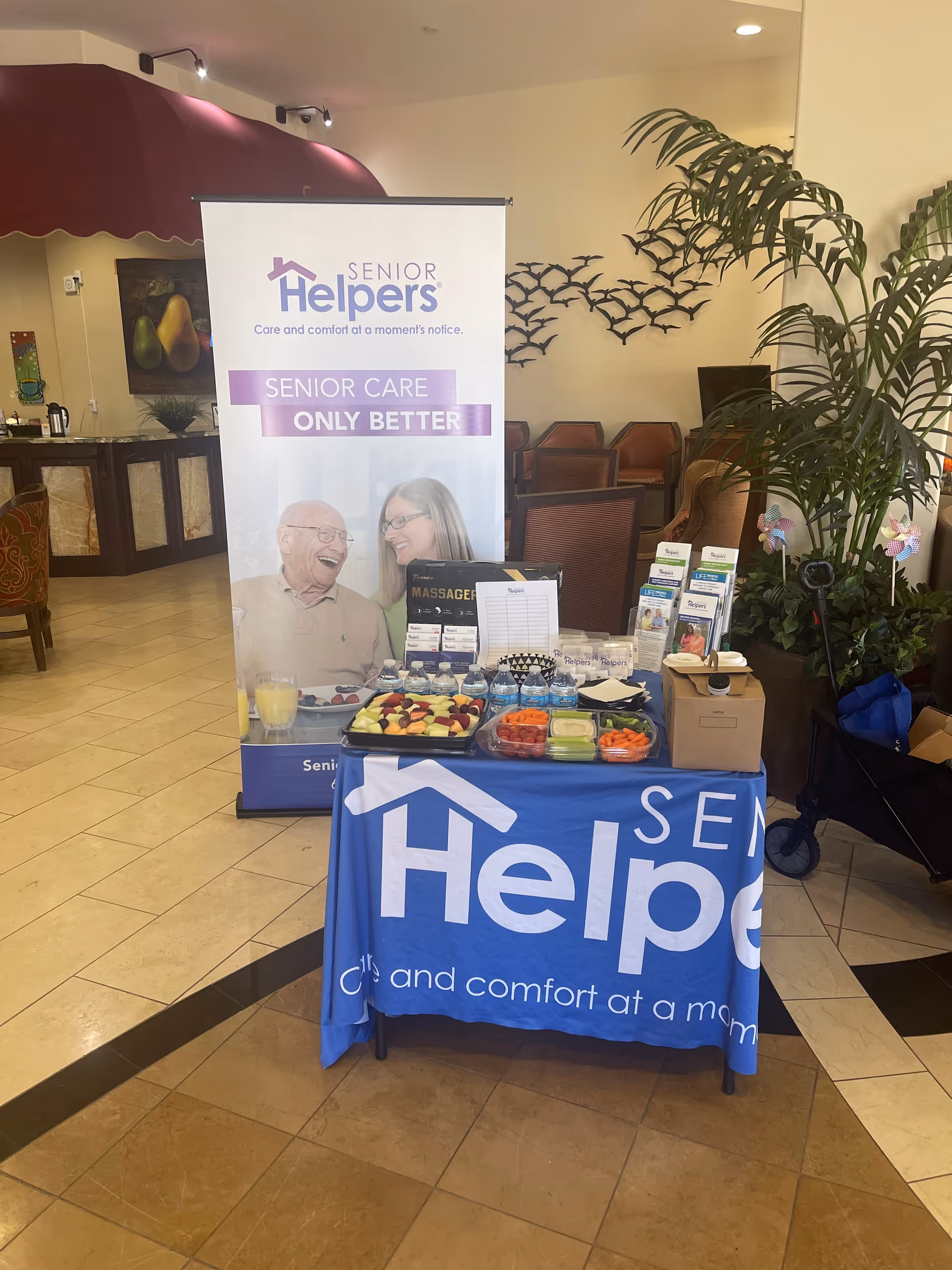 Lobby area with a Senior Helpers banner behind a table of snacks and brochures.
