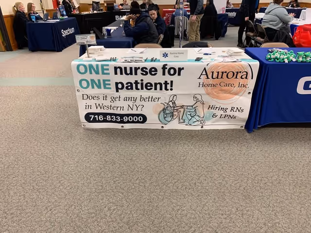 Indoor expo booth for Aurora Home Care with banner reading 'One nurse for one patient'.