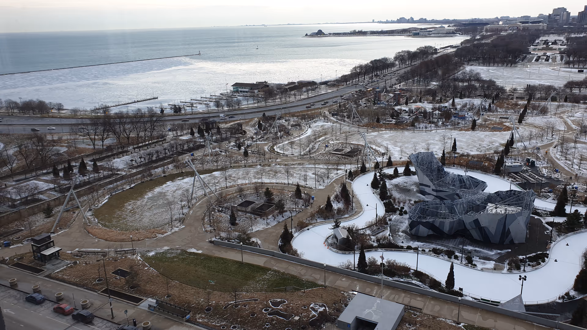 An aerial view of a snow-covered coastal park with a large angular building.