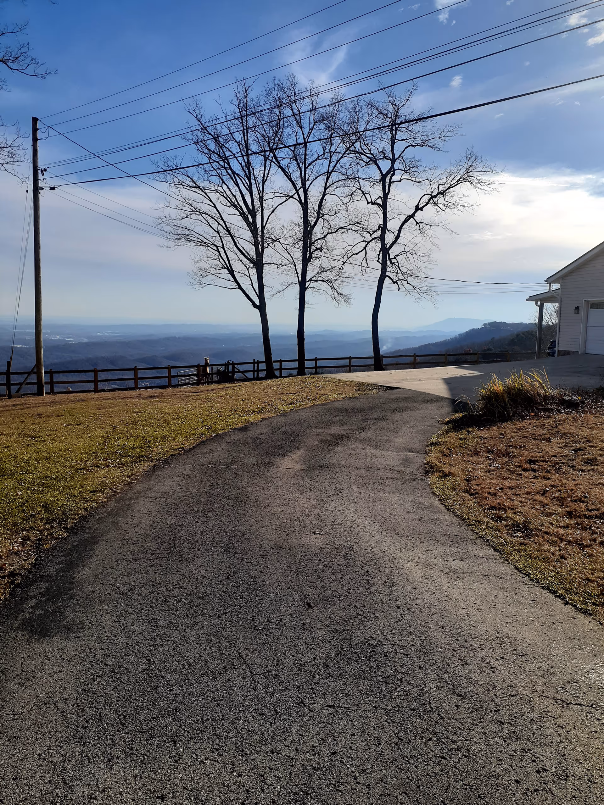 Winding asphalt driveway toward a white building with bare trees and mountain view.