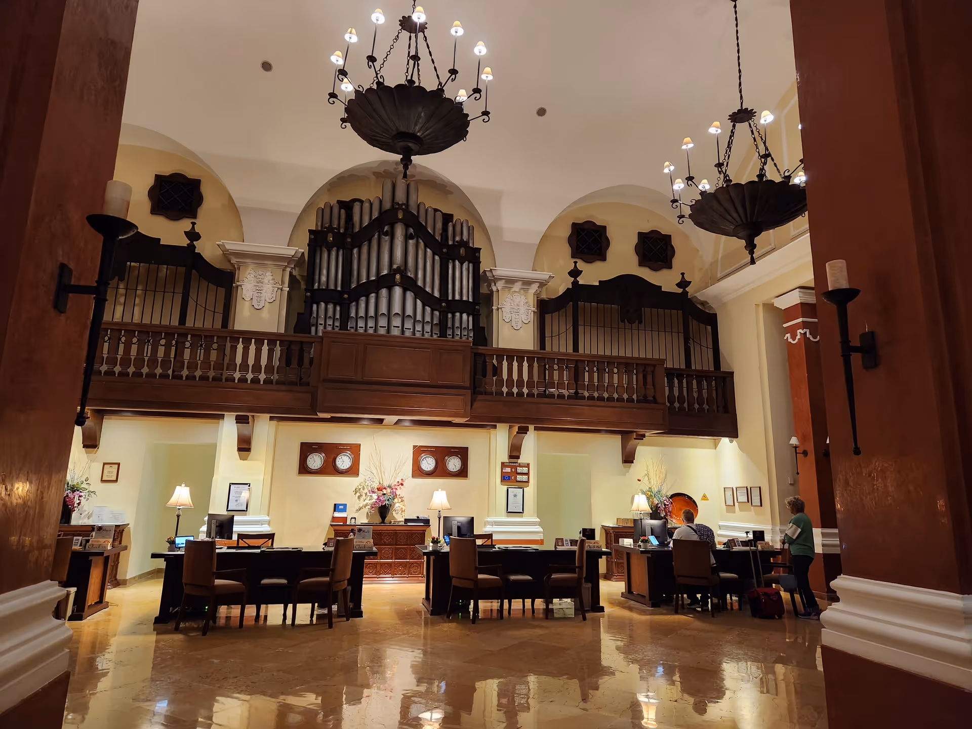 Grand lobby with a large organ, chandeliers, and reception desks in a spacious hall.