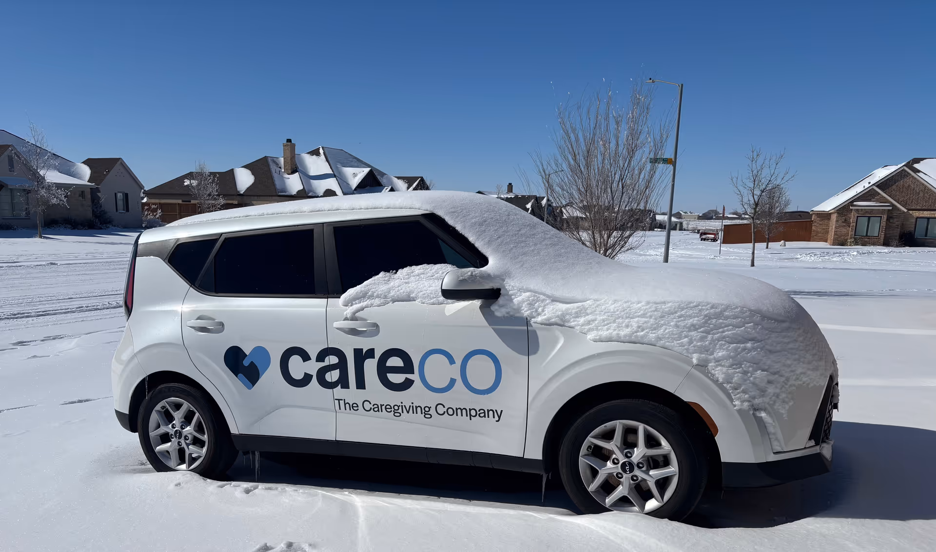 Snow-covered white CareCo van parked on a residential street with houses in the background.