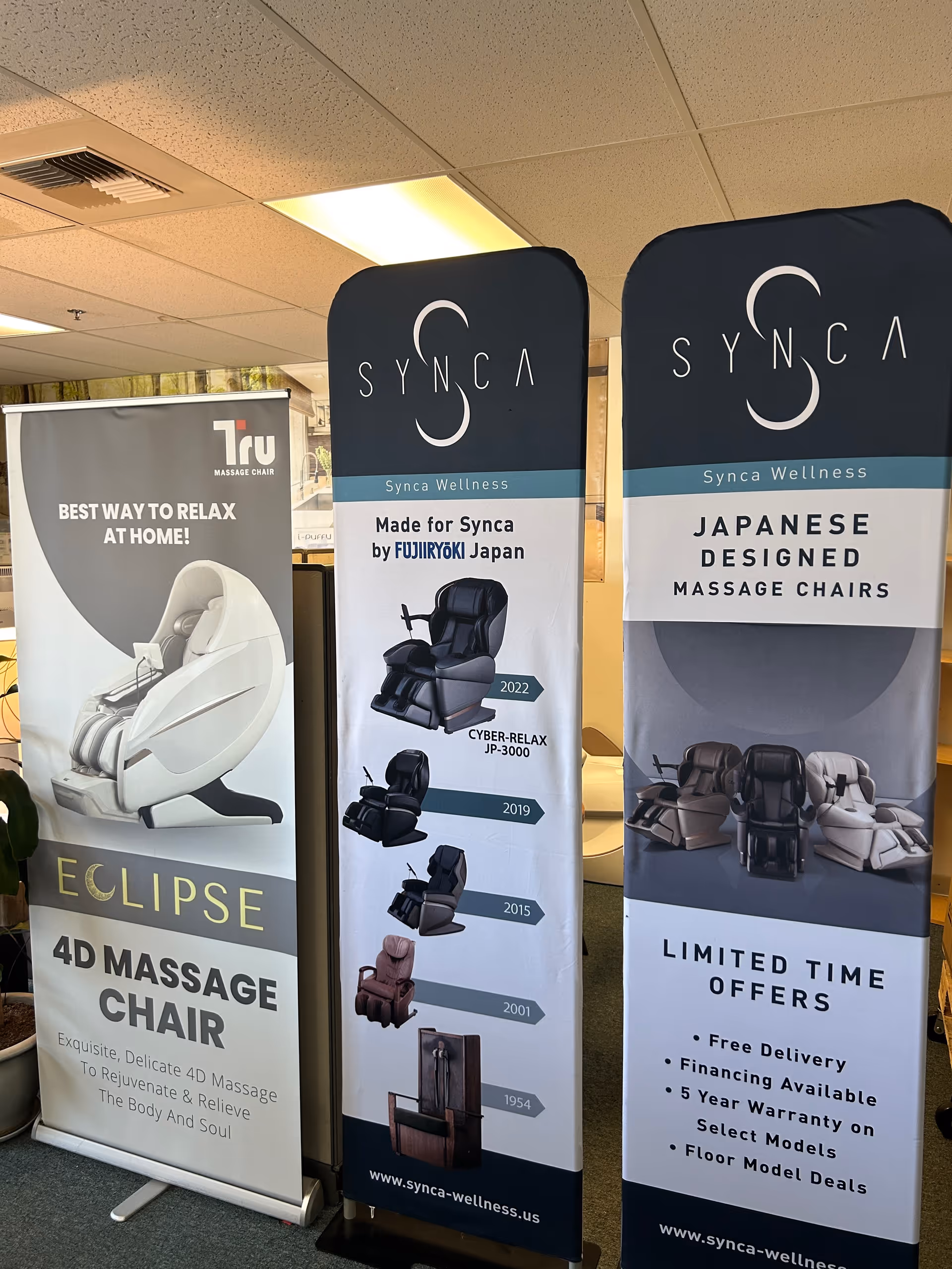Indoor showroom with vertical banners advertising Synca massage chairs.