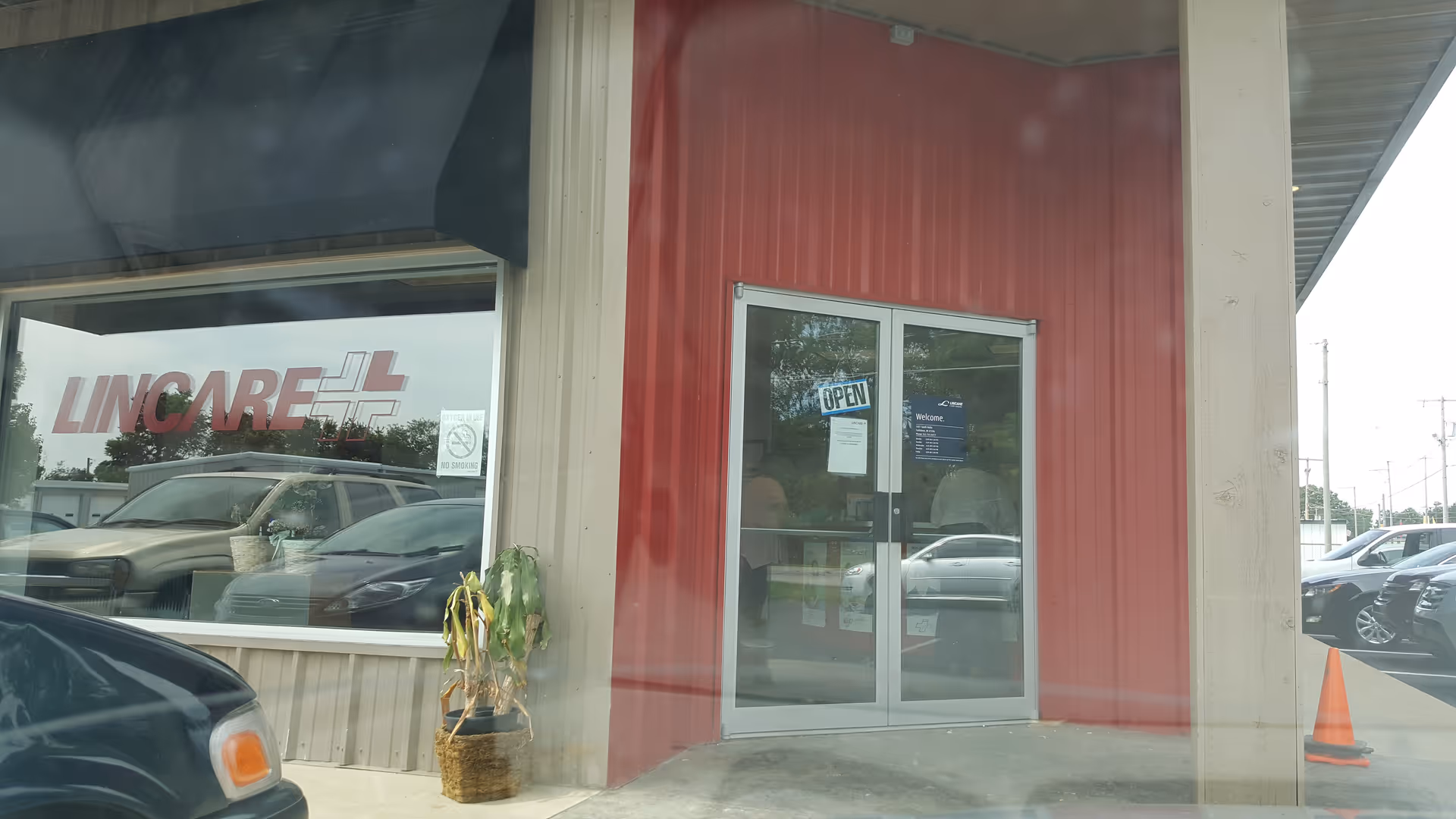 Exterior view of LINCARE facility entrance with glass doors, red facade, and parked cars.