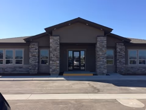 Front entrance of a modern single-story building with stone pillars and glass doors.
