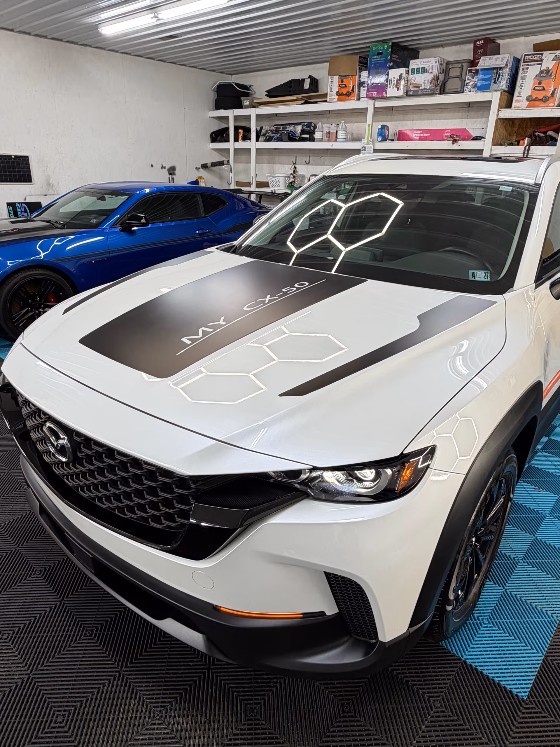 White SUV with hexagonal decals parked in a garage beside a blue sports car