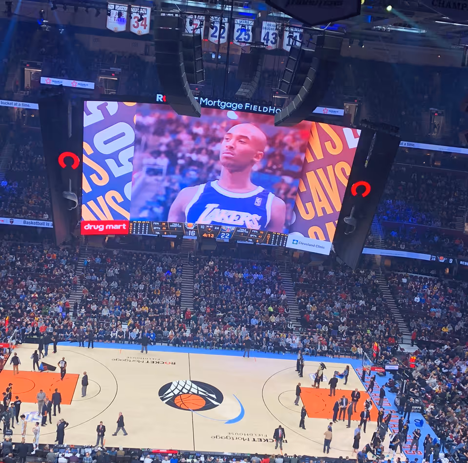 A packed basketball arena with a large video screen showing an athlete during a game.