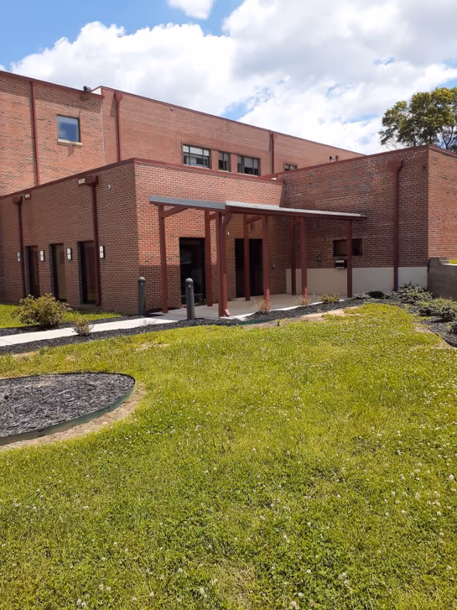 Brick facility exterior featuring a covered entrance and surrounding green lawn.