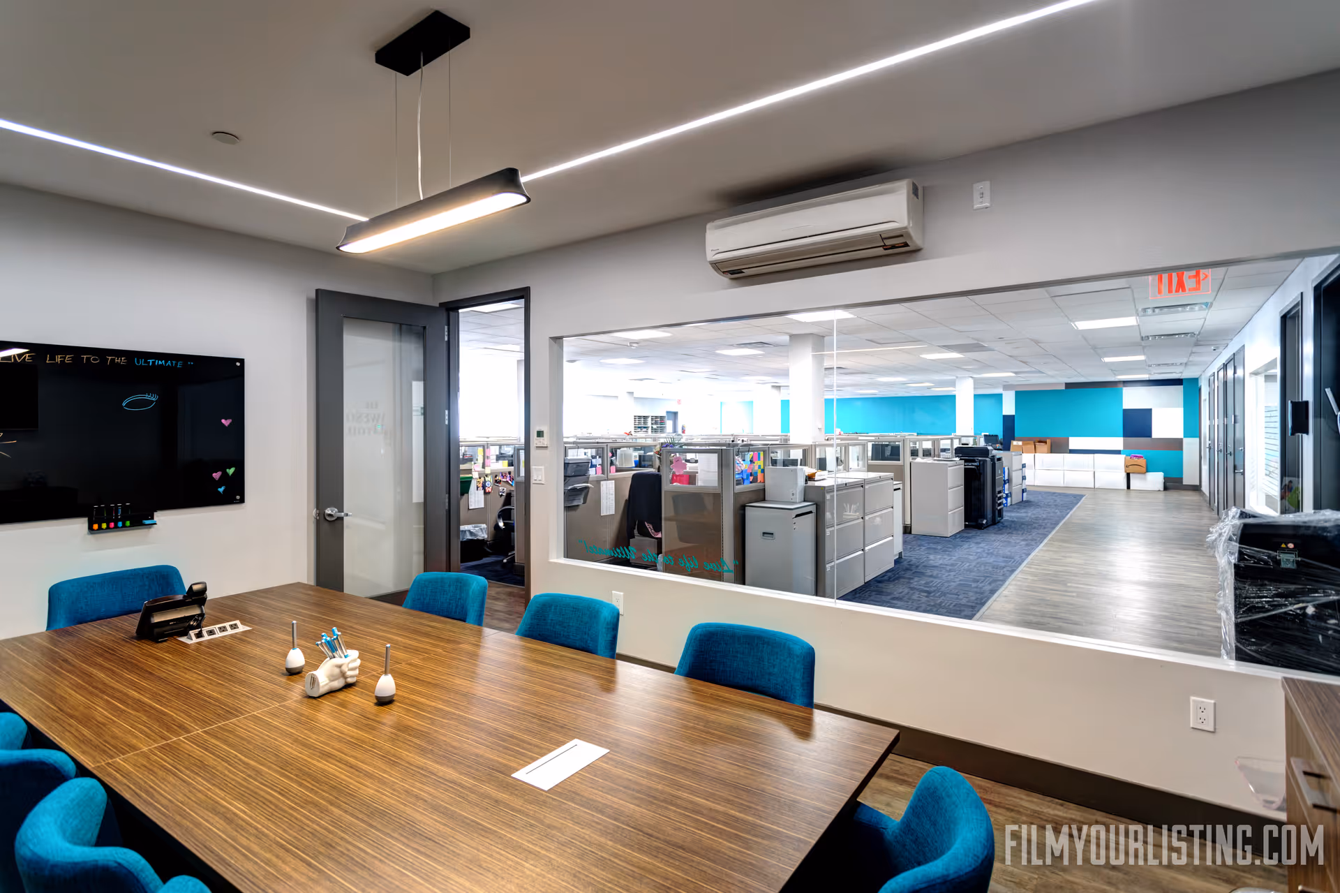 Wooden conference table with blue chairs inside a glass-walled office space.
