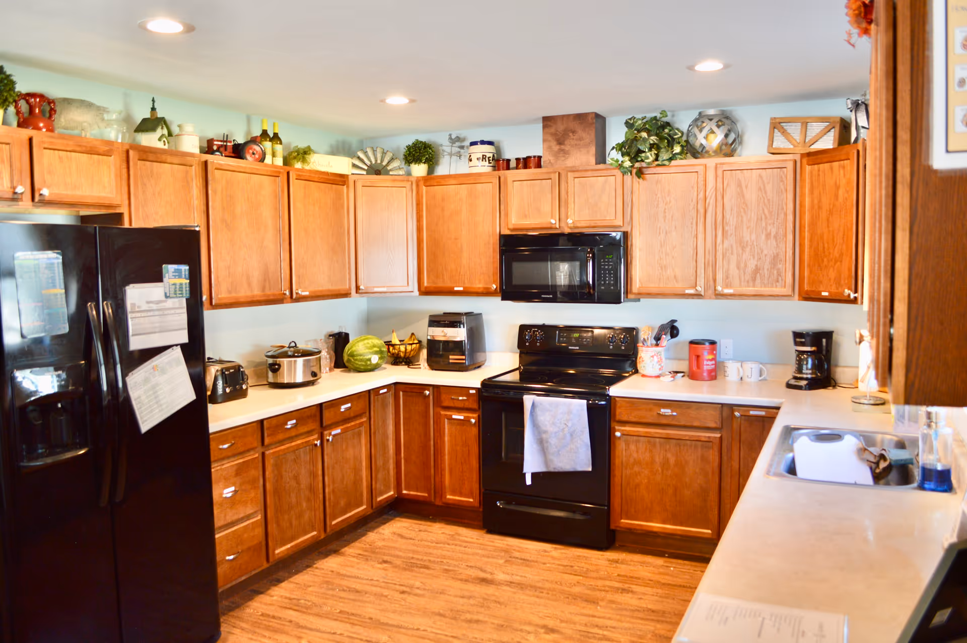U-shaped kitchen with wooden cabinets, black appliances, and small countertop gadgets along a bright wall.