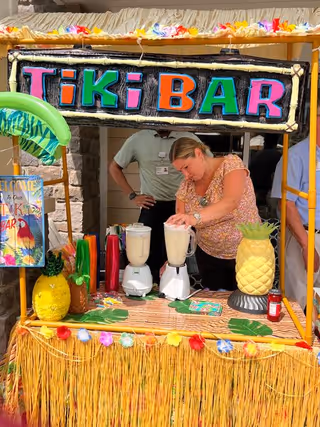 Staff blends drinks at a tropical tiki bar display during a facility event.