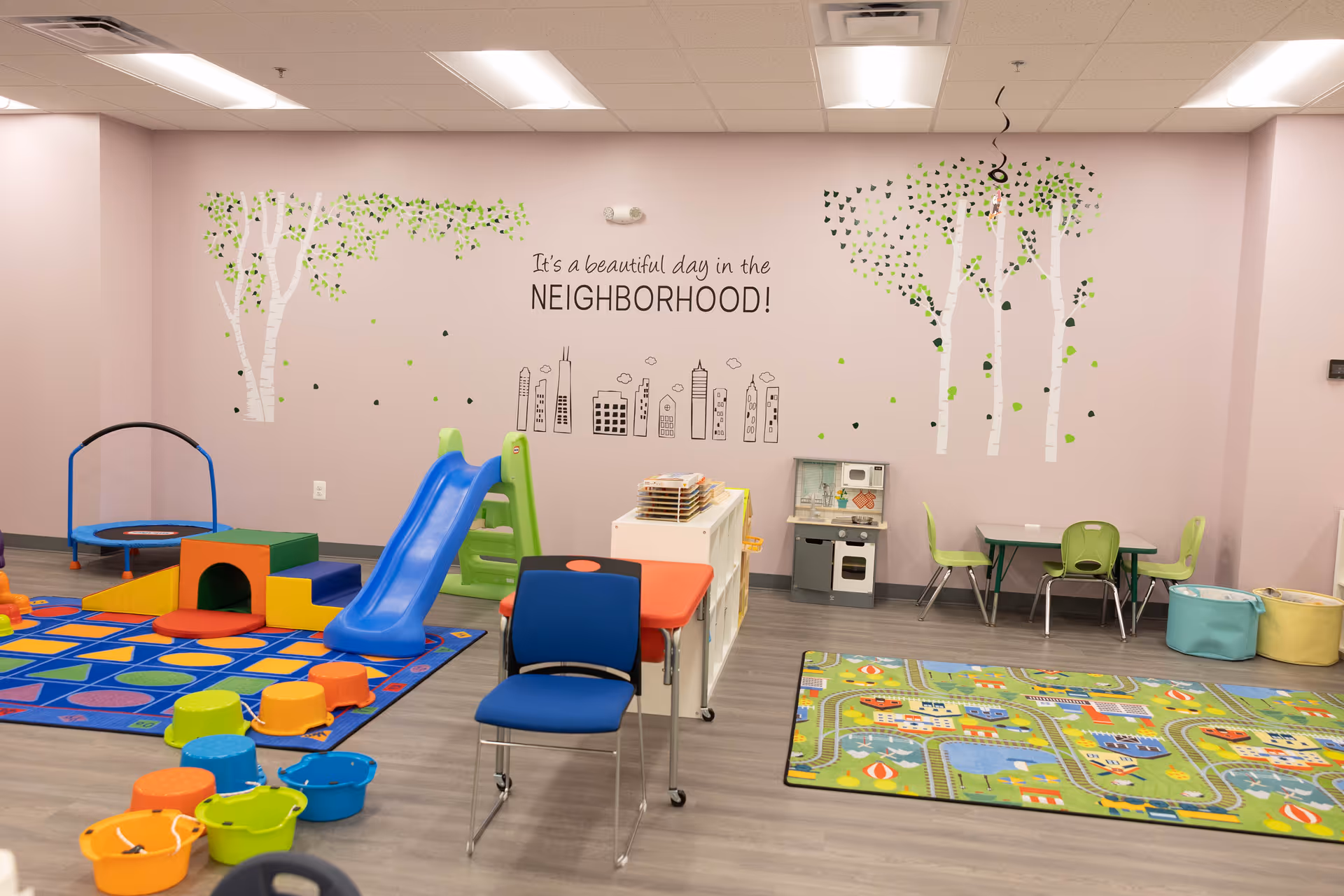 Colorful children's play area with slide, mats, and small furniture inside a pink-walled room.