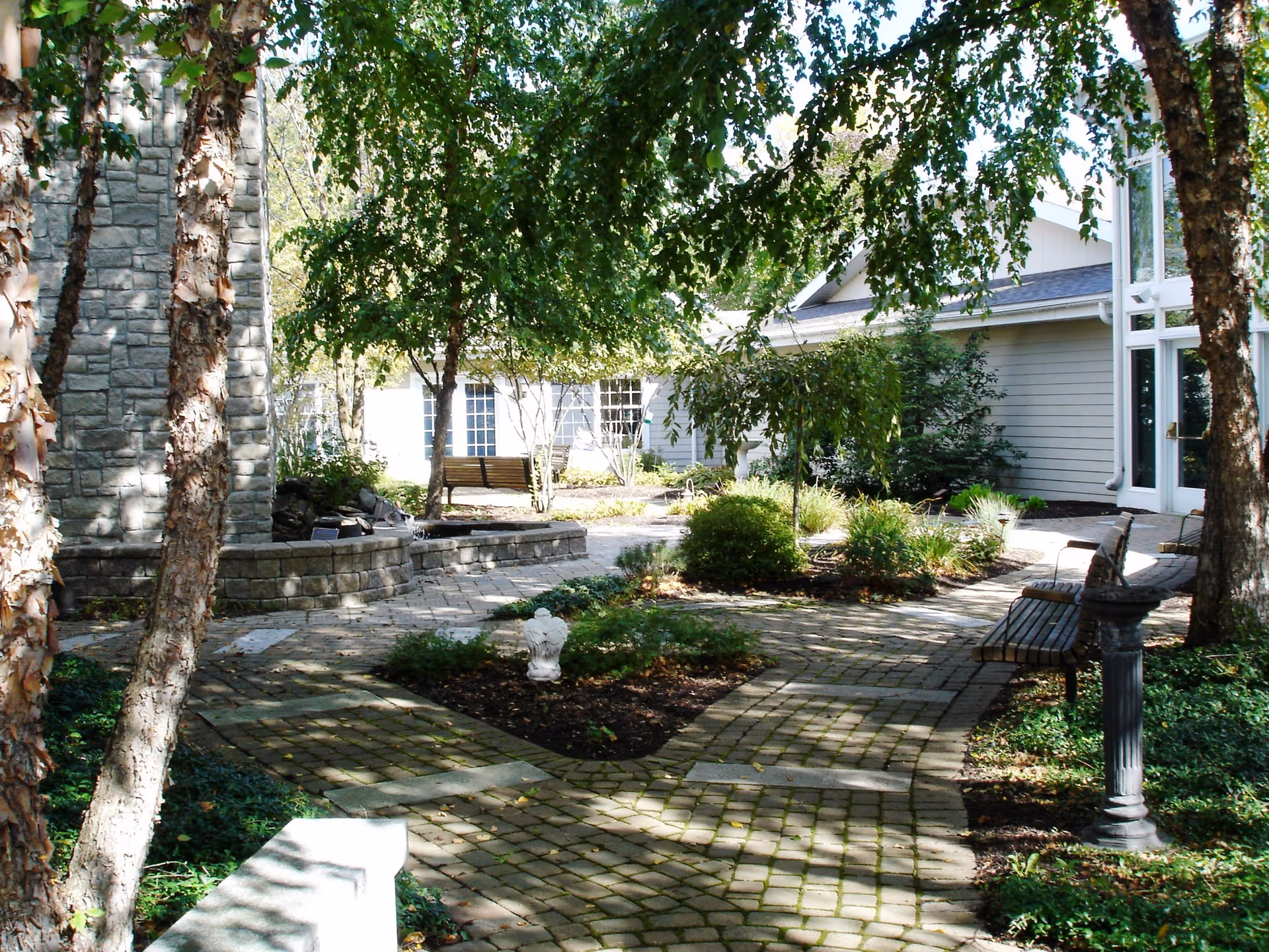 Stone-paved courtyard with benches, trees, and a building entrance in a tranquil garden.