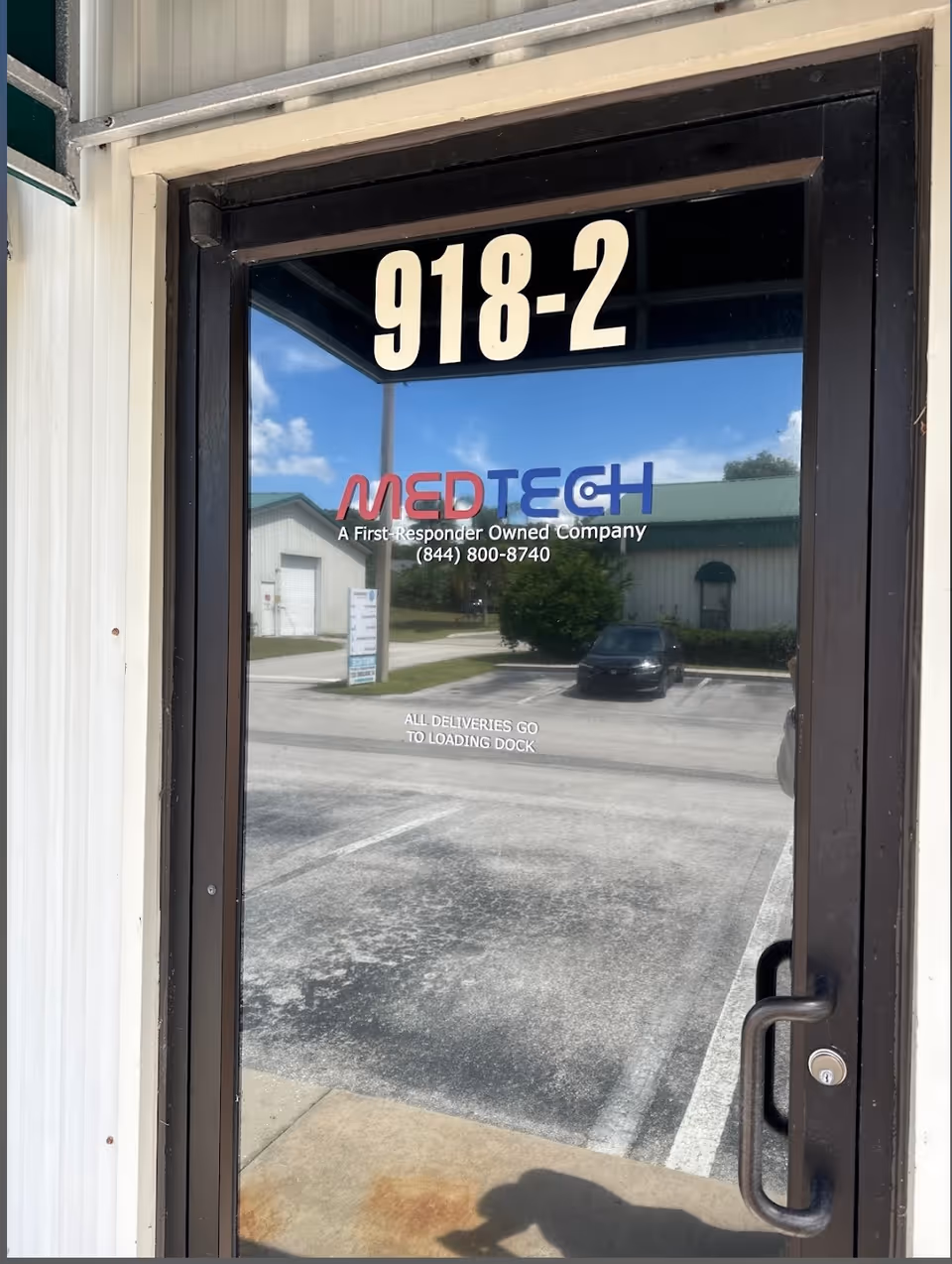 Glass door with 918-2 address and MEDTECH logo reflecting a parking lot.