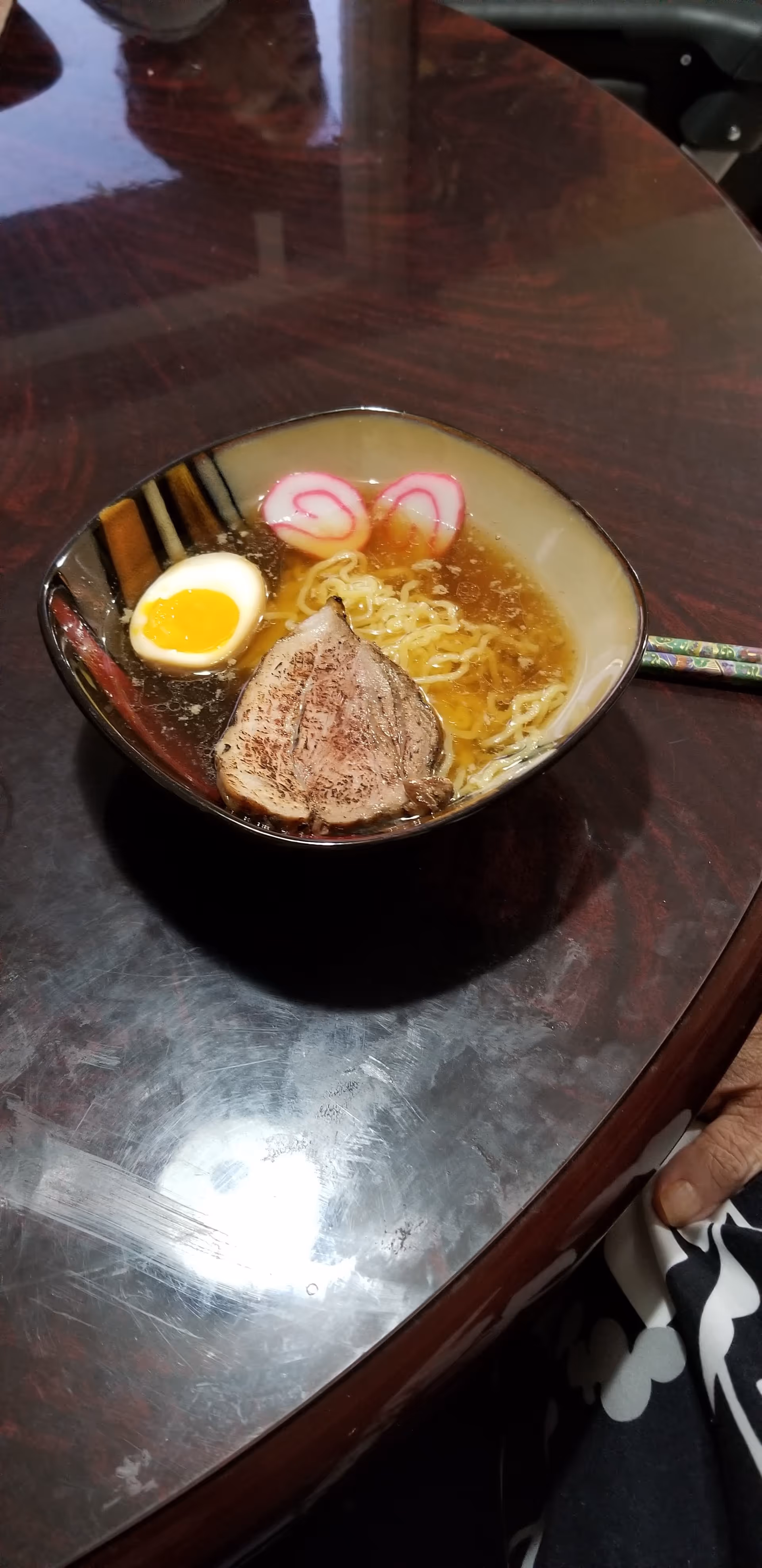 A bowl of ramen with egg and pork on a dark wooden dining table.