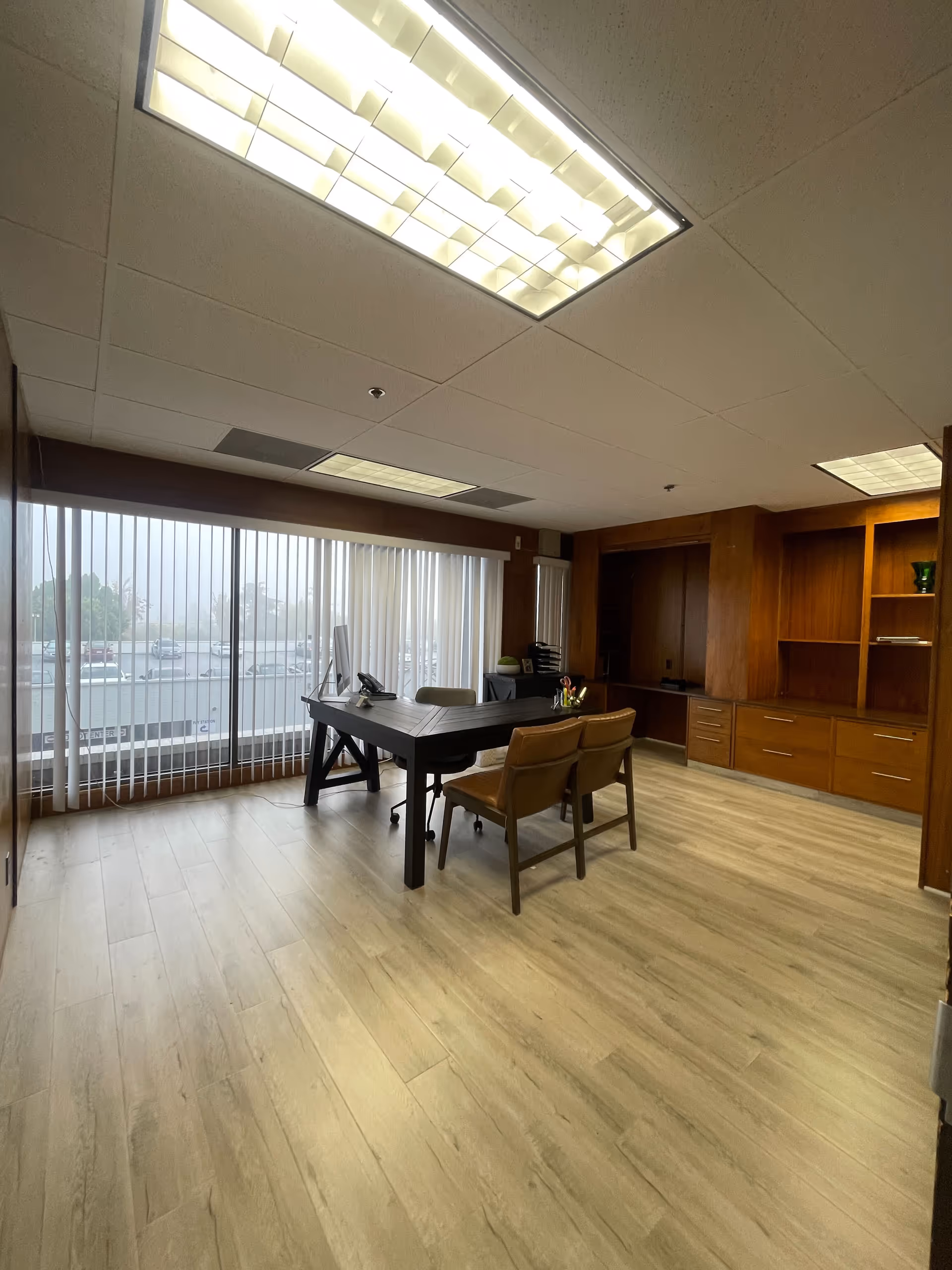 Office-like conference room with a dark desk, chairs, and wooden cabinets along the windows.