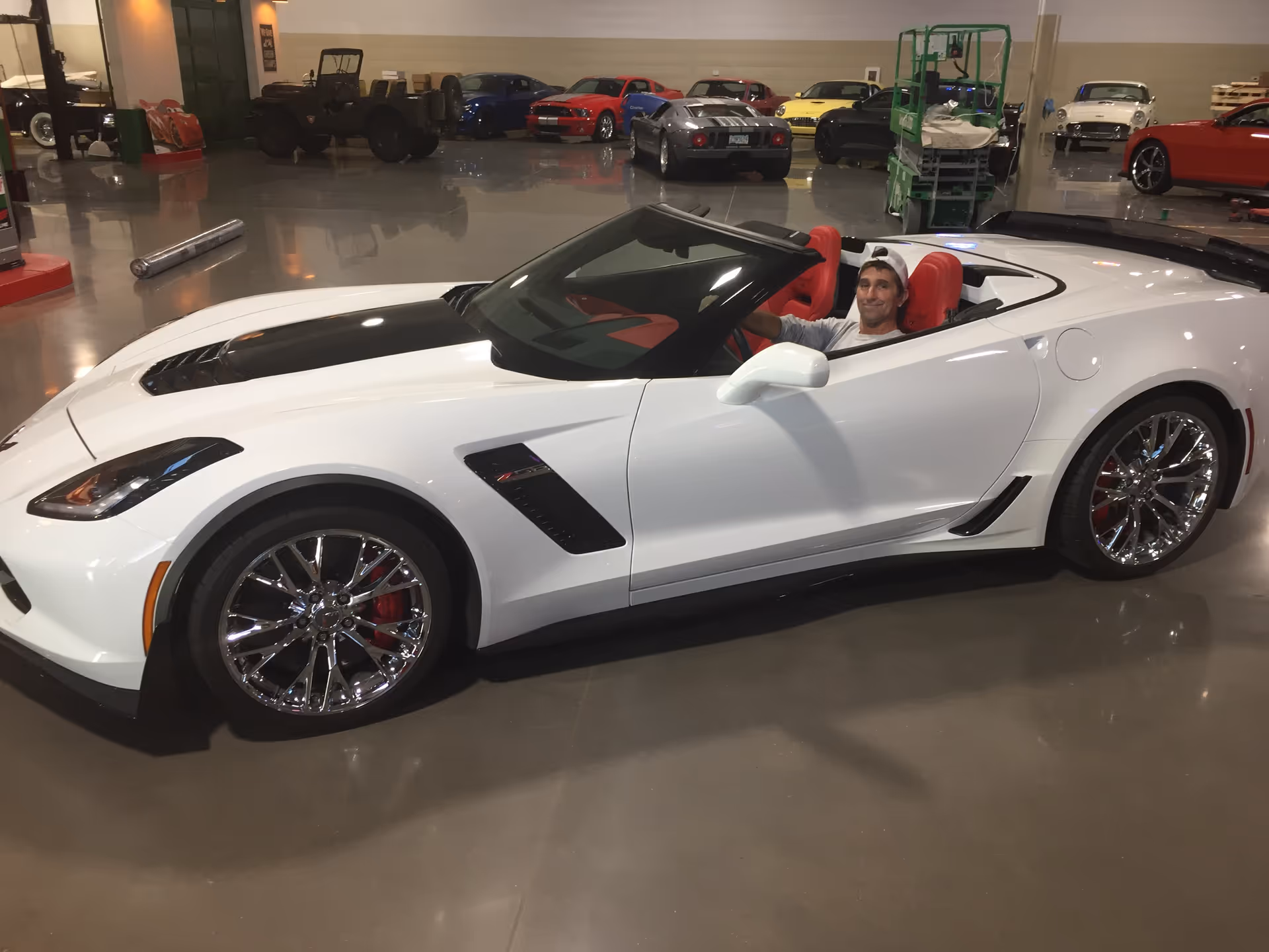 White convertible sports car inside a showroom with a man seated in the driver's seat.