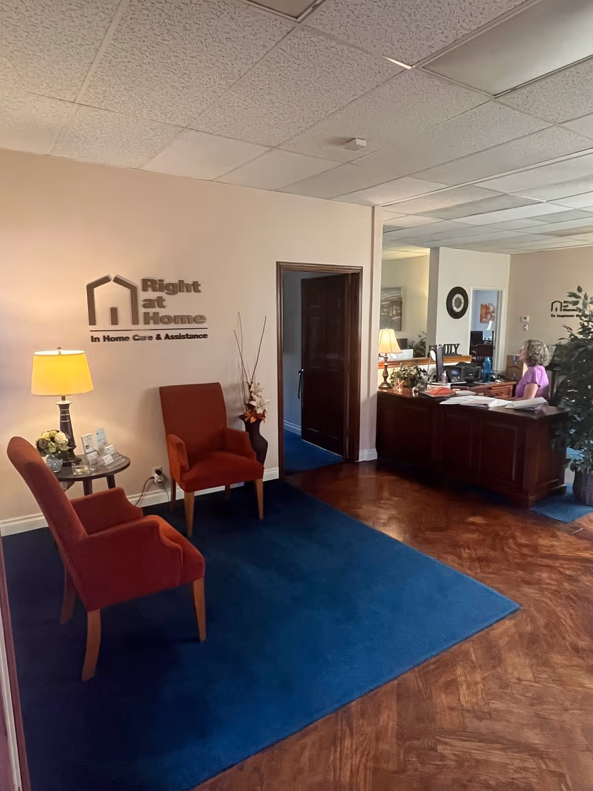 Reception area of Right at Home facility with two red chairs and a staffed front desk.