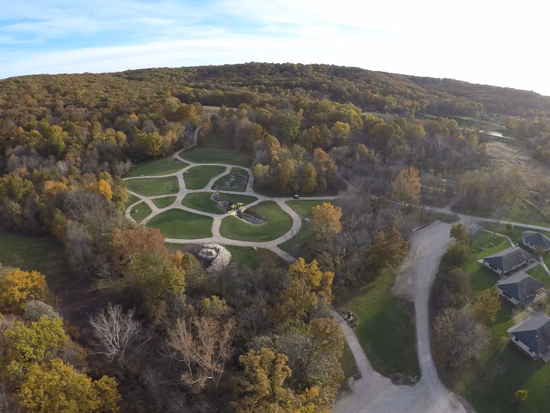 Aerial view of winding garden paths through a wooded campus landscape with nearby buildings.