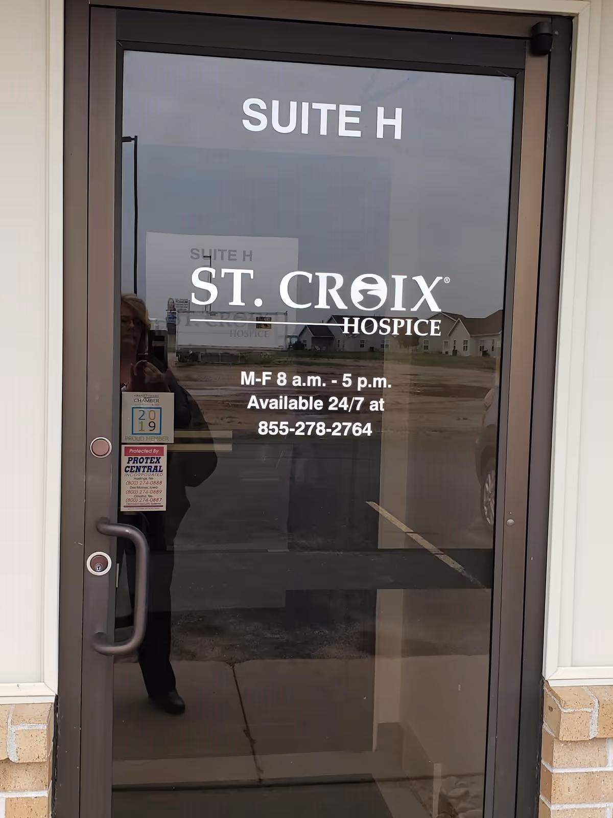 Glass entry door for St. Croix Hospice Suite H with reflections of the parking lot.