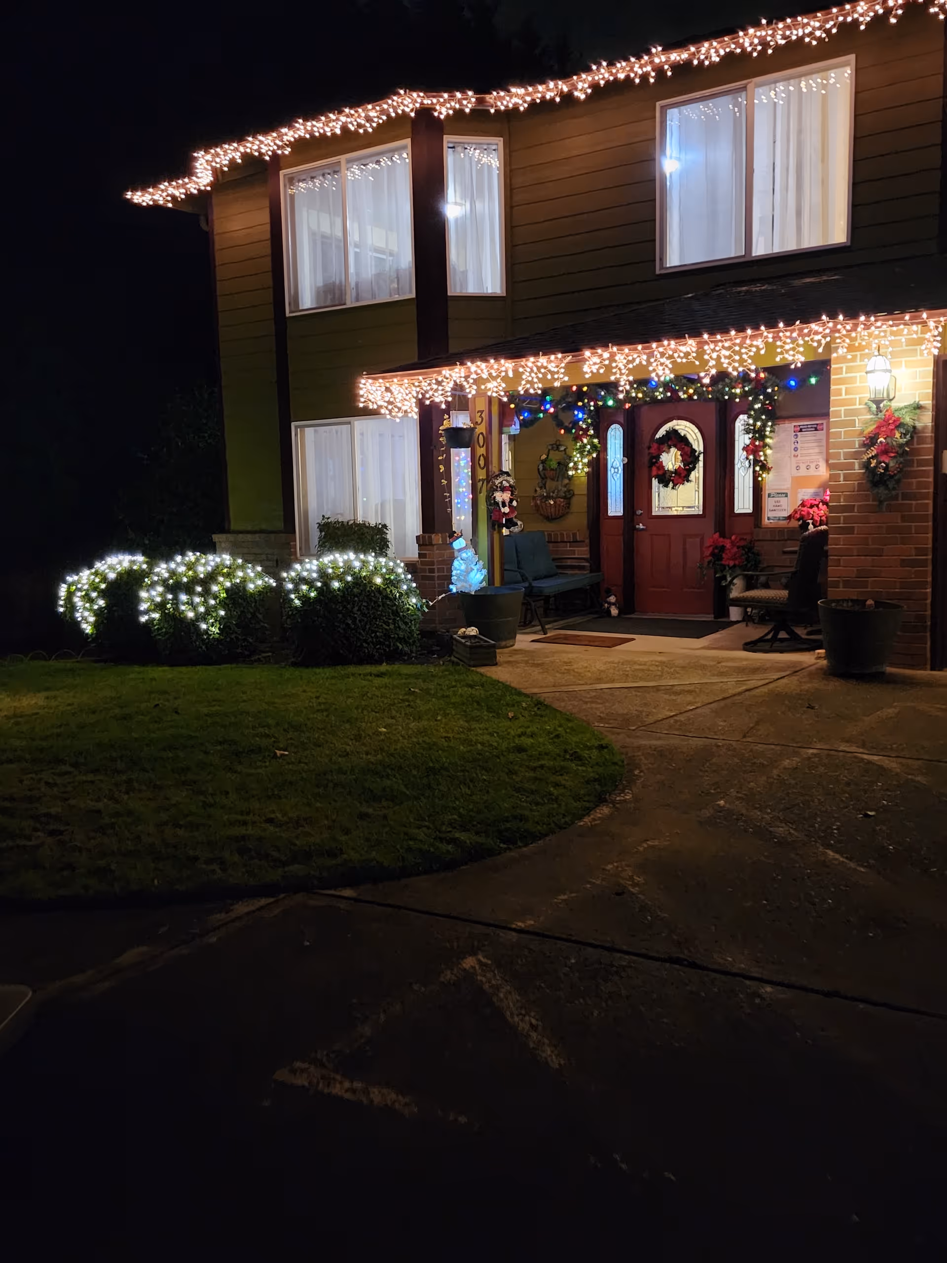 Two-story senior living home exterior at night with festive holiday lights and wreaths.