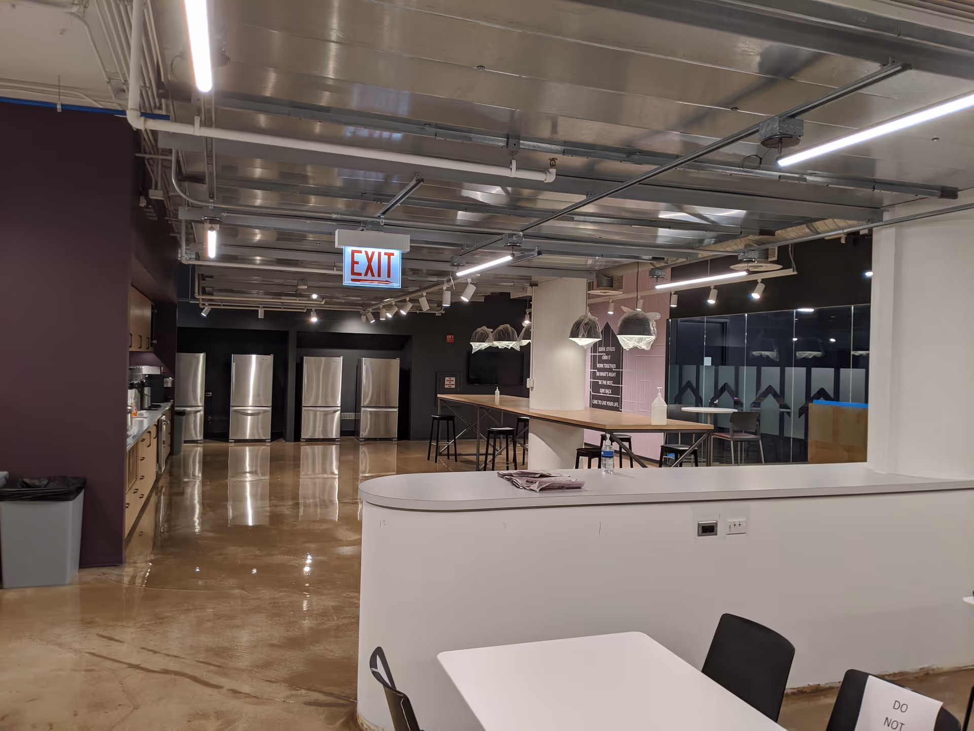 Industrial kitchen area with stainless steel appliances, counter seating, and an exit sign visible.