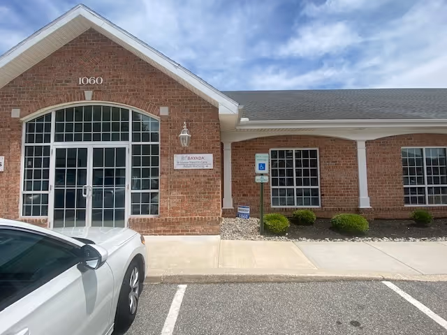 Brick senior living facility exterior with arched glass doors and a parked white car.