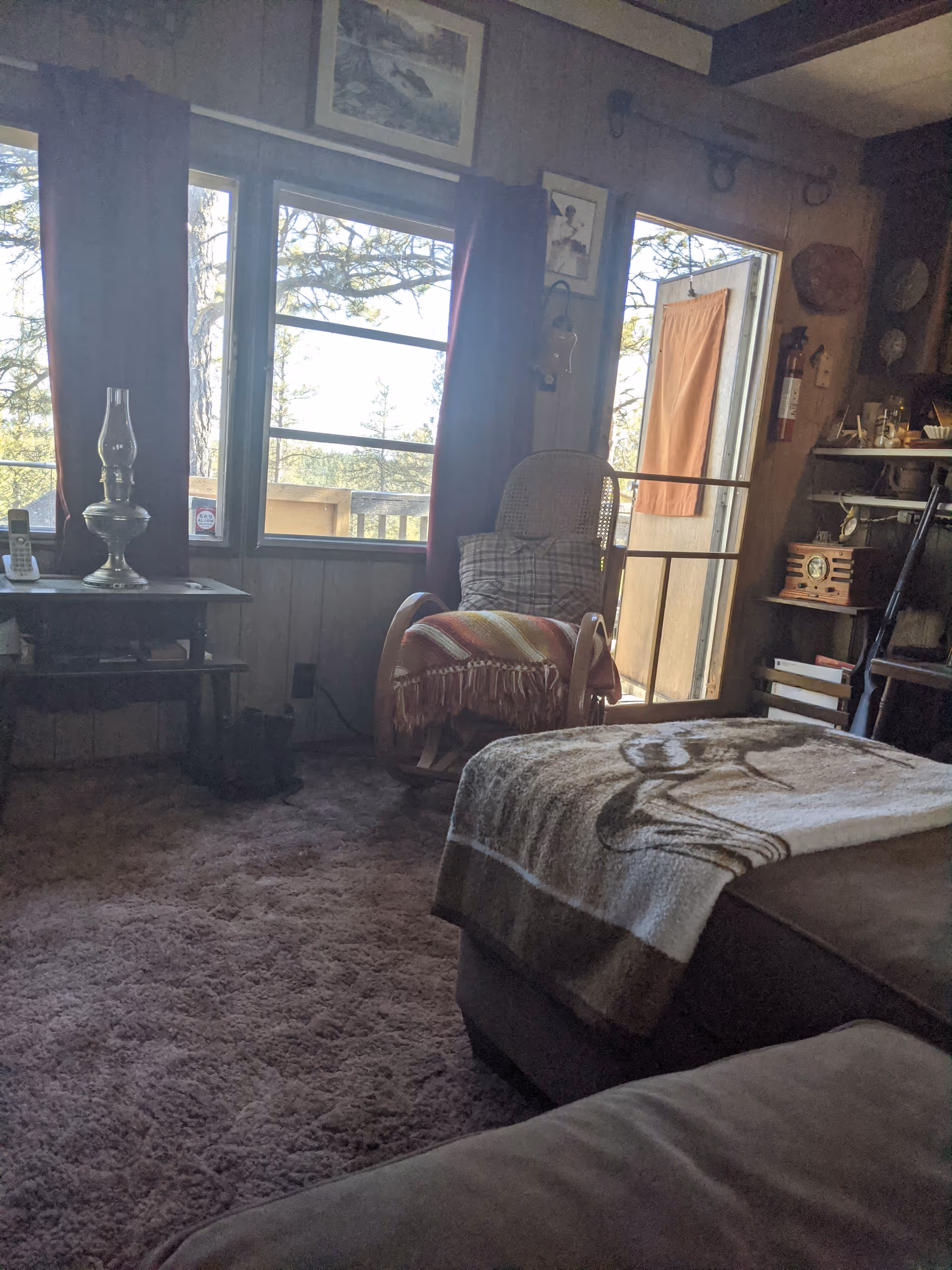 Cozy living room with window view, rocking chair, lamp, blanket, and shelves.